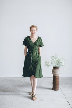 a woman in a green dress standing next to a vase with white flowers on it