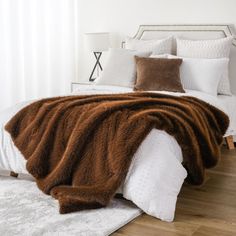 a bed with white and brown blankets on it's headboard in a bedroom