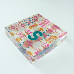 a clear box with a blue letter on the inside and colorful paint splatters all over it