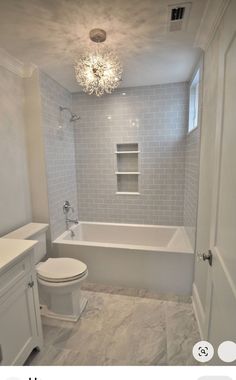 a bathroom with white fixtures and gray tile on the walls, along with a chandelier