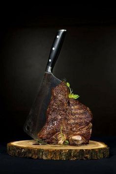 a piece of meat with a knife stuck in it on a wooden board next to a black background