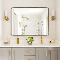 a white bathroom with gold accents and a large mirror over the sink that has a vase on it