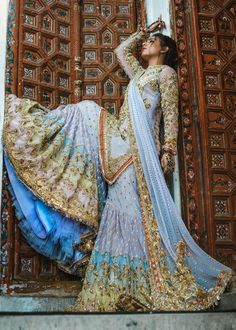 a woman in a blue and gold dress standing next to a wooden door with her hands on her head