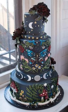 a three tiered cake decorated with flowers and butterflies on a table next to a window