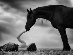 a woman laying on the ground next to a horse and holding her hand up in front of it