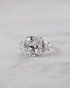 an oval and baguette cut diamond ring on a white marble surface with three side stones