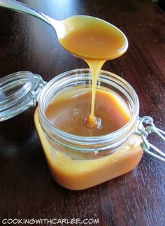 a spoon full of orange sauce sitting on top of a wooden table next to a jar