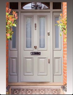 a grey front door with two potted plants on either side and brick wall behind it