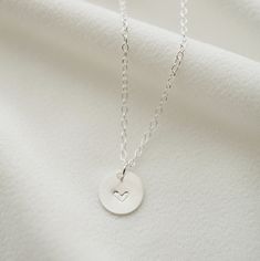 "A dainty silver coin is delicately suspended on a sterling silver necklace chain, and hand stamped with an uppercase letter of your choice. Add on additional coins personalized with letters of your choice, or a heart symbol. Hand stamped to order in our Vancouver studio. *Free shipping for orders to USA and Canada, and no duties or customs fees.* > Sterling silver coin is 9mm in diameter > Shown worn on a 16\" satellite chain > Comes beautifully packaged and ready for gift giving > Minimalist Hand Stamped Charm Necklace As Gift, Dainty Hand Stamped Charm Necklace For Anniversary, Dainty Hand-stamped Charm Necklace For Anniversary, Anniversary Dainty Hand-stamped Charm Necklace, Dainty Hand Stamped Charm Necklaces For Everyday, Dainty Hand Stamped Charm Necklace For Everyday, Dainty Hand Stamped Everyday Jewelry, Dainty Hand Stamped Jewelry For Everyday, Dainty Hand Stamped Round Pendant Necklaces