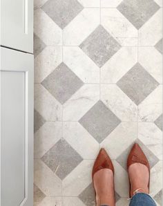 a woman's legs in high heels standing on a tile floor next to a cabinet