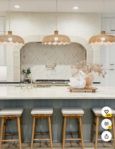 a kitchen with four stools in front of an island and three lights above it