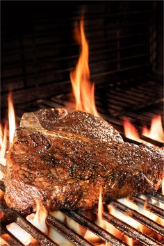 a steak is cooking on the grill with flames