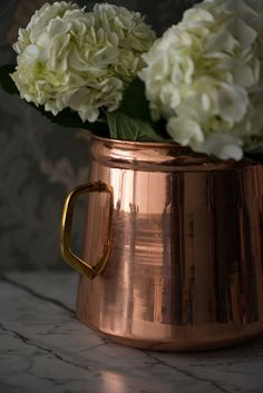 some white flowers in a copper vase on a marble counter top with a gold handle