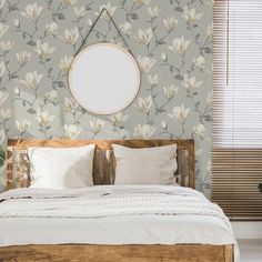 a bed with white sheets and pillows in front of a floral wallpaper