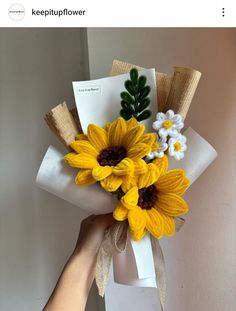 a hand holding a bouquet of yellow and white sunflowers on top of a piece of paper