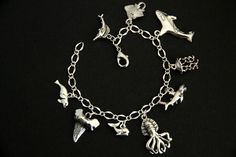 A collection of silver plated marine life themed charms have been dispersed around a shimmering silver plated bracelet chain in this handmade charm bracelet. This sea predator charm bracelet is then completed with a lobster clasp and a 1/2 inch of chain at the end for adjustable sizing. Charms in this bracelet include a seal charm, shark tooth charm, whale charm, octopus charm, shark charm, jellyfish charm, orca charm, stingray charm, and swordfish charm. ● Sizing ● To determine your bracelet si Themed Sterling Silver Charms, Personalized Silver Novelty Bracelets, Personalized Novelty Silver Bracelets, Themed Silver Charm Bracelet, Themed Silver Sterling Charms, Personalized Novelty Silver Bracelet, Silver Novelty Metal Charm Bracelet, Silver Novelty Charm Bracelet, Silver Novelty Bracelets With Charms