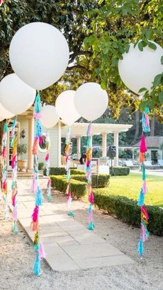 some balloons are hanging from the trees in front of a house with white balls and tassels