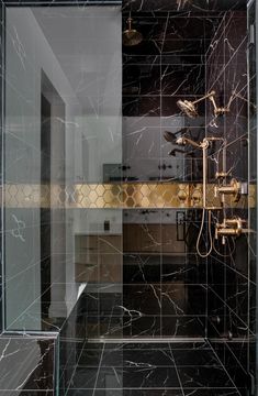 a bathroom with black marble walls and flooring is shown in this image, there are gold fixtures on the shower head