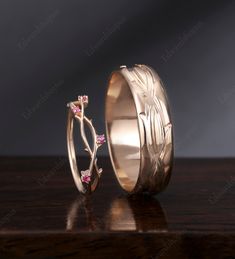 two gold wedding bands with pink sapphire flowers on the inside and outside, sitting on a wooden surface