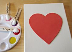 a heart shaped paper cut out on a canvas next to paintbrushes