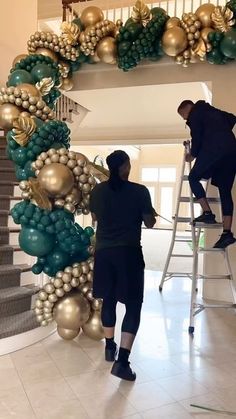 two men are decorating a christmas tree with gold and green ornaments on the stairs