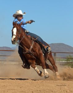 a woman riding on the back of a brown horse in a dirt field next to a fence