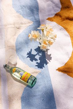 an empty bottle sitting on top of a beach towel next to a flower vase with white flowers in it