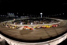 a group of cars driving around a track at night