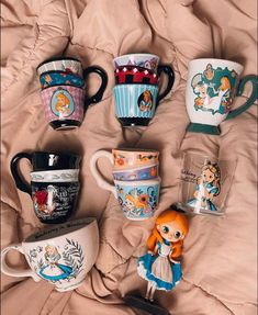 there are many coffee mugs on the bed and one has a doll in it