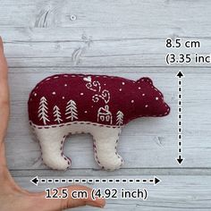 a hand holding a stuffed bear with trees on it's back and measurements for the size