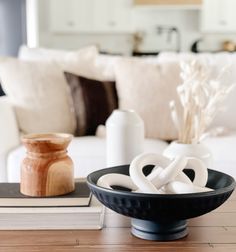 a black bowl sitting on top of a wooden table next to a book and vase