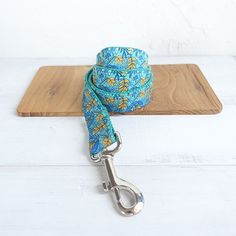 a blue and yellow flowered dog leash on a wooden board with a metal hook