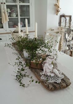 an arrangement of plants and candles on a table in a room with white furniture,