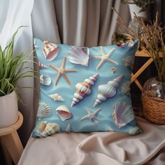 a blue pillow with sea shells on it next to a potted plant and window