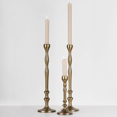 two brass candlesticks with one lit and the other turned off, on a white surface