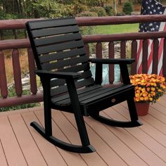 a wooden rocking chair sitting on top of a deck next to a flower pot with an american flag in the background