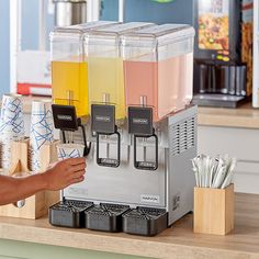 a person is filling up drinks from a small machine on a counter top with other items