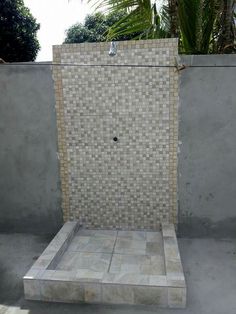 a walk in shower sitting on top of a tiled floor next to a cement wall