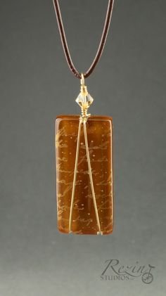 "Caramel brown glass is accented with golden script and gold wire wrapping to create this elegant handmade fused glass necklace. Glass pendant is kiln fired, shaped, and fire-polished in my glass studio. Glass pendant is wire wrapped with gold-plated wire, accented with a gold-colored Swarovski crystal bead, and hangs from a brown leather necklace with a sterling silver lobster clasp. Pendant is .75\" x 2.25\" including bail. Necklace is 18\"." Gold Wire Wrapped Glass Necklaces, Elegant Gold Necklace With Copper Wire, Gold Glass Jewelry Wire Wrapped, Brown Leather Necklace, Fused Glass Necklace, Jewelry Board, Glass Studio, Fused Glass Jewelry, Jewelry Boards