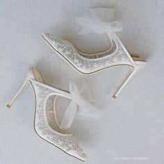 two pairs of white high heels with bows on the toes and one shoe is decorated with sequins