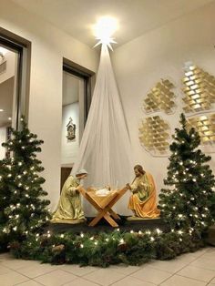 two nativity figures sitting at a table surrounded by christmas trees with lights on them