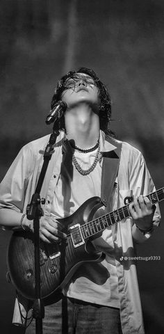 a man holding a guitar while standing in front of a microphone with his eyes closed