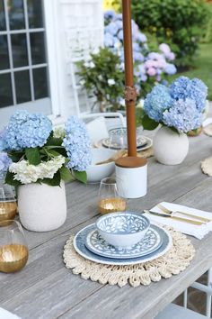 a wooden table topped with plates and vases filled with blue hydrangea flowers