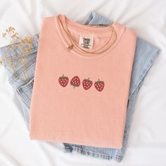 Welcome the sunny days with our delightful Summer Strawberry Embroidered T-Shirt! Made from 100% cotton, this t-shirt is not only comfortable but also perfect for staying cool during warm weather. Available in sizes S to 2XL and nine vibrant colors including Banana, Bay, Blossom, Butter, Chalky Mint, Chambray, Ivory, Orchid, and Peachy, there's a shade to suit every style.The standout feature of this t-shirt is the charming summer fruit-inspired design, showcasing four intricately embroidered strawberries on the center chest. Whether you're heading to a picnic, beach outing, or simply enjoying a leisurely day, this t-shirt adds a touch of sweetness to your summer wardrobe.Please note that colors may vary slightly due to monitor settings. For accurate sizing, refer to the size charts provid Trendy Embroidered Summer T-shirt, Cute Organic Cotton T-shirt For Everyday, Casual Embroidered Organic Cotton Tops, Pink T-shirt With Embroidered Text For Summer, Pink Embroidered T-shirt For Summer, Everyday Cotton T-shirt With Embroidered Graphics, Pink Embroidered Cotton T-shirt, Summer Everyday T-shirt With Embroidered Text, Trendy Summer T-shirt With Embroidered Text