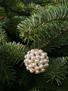 a christmas ornament hanging from a pine tree with white pearls and red crystals