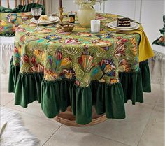 a table covered in green and yellow cloths with plates on top of it next to a vase filled with flowers