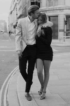 a man and woman walking down the street in front of a traffic light, with their arms around each other