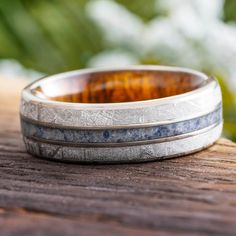 two wedding bands with wood inlays are sitting on a piece of wood outside