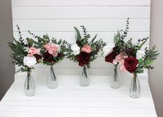 three vases with flowers in them sitting on a white shelf next to each other