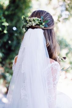 the back of a bride's head wearing a veil with flowers and greenery